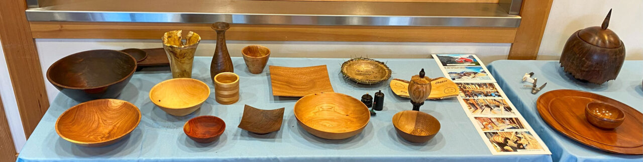 A table full of various woodturned items. Mostly bowls, vases, and platters. The photo is for woodturners newsletter.
