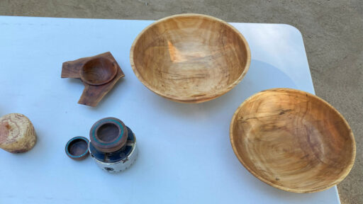 Two large bowls, and other woodturning projects. A lathe chuck holds a small bowl with stone inlay.