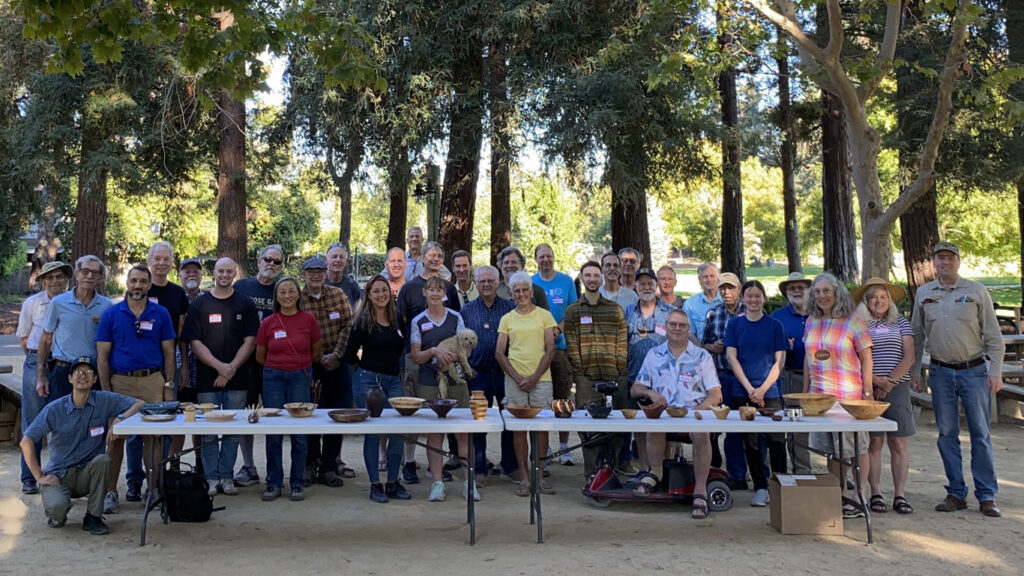 A group of people with a table full of woodturning projects. The photo of WBW and SVW members was taken for the woodturners newsletter.