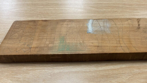A wooden board with carved grooves showing various designs.