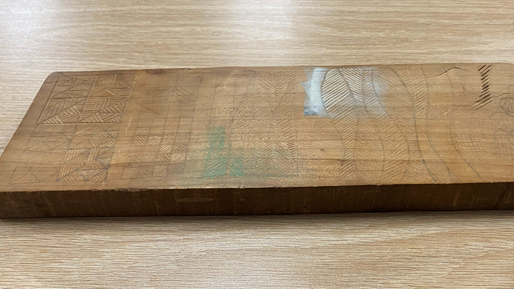 A wooden board with carved grooves showing various designs.