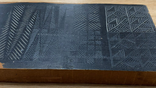 A wooden board with carved grooves showing various designs.
