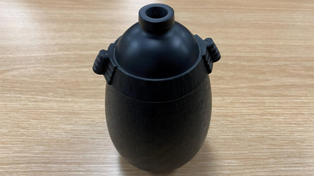 A turned vessel with carved handles and embellished walls with repetitive grooves.