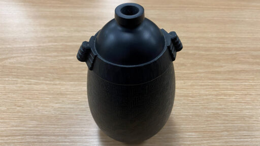 A turned vessel with carved handles and embellished walls with repetitive grooves.