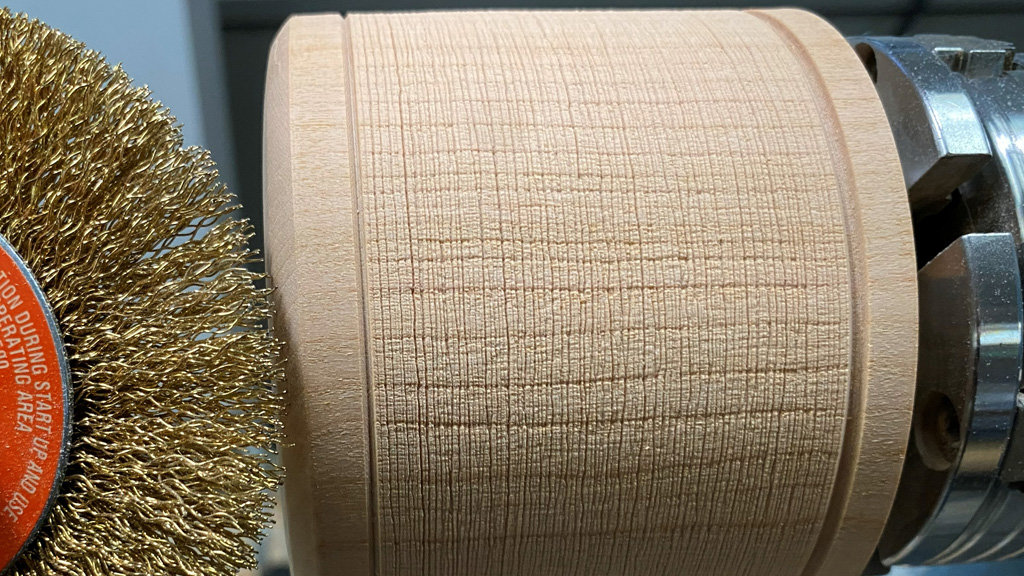 A piece of wood is mounted on a lathe and embellished with a wire-brush.