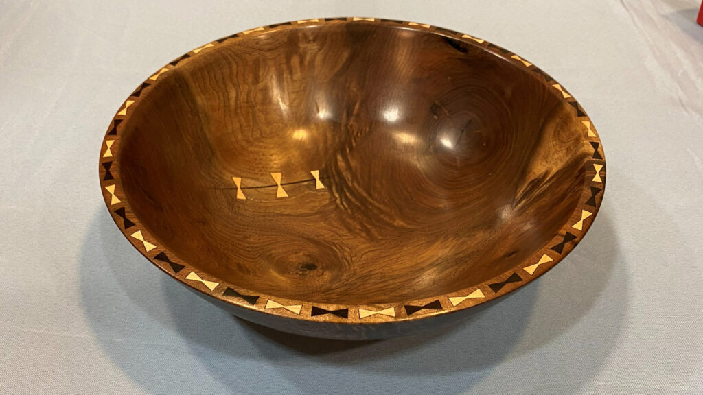 A gorgeous walnut bowl turned and decorated with bow ties on the rim by Chip. It has a small crack at the bottom, reinforced with three bowties.