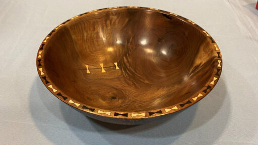 A gorgeous walnut bowl turned and decorated with bow ties on the rim by Chip. It has a small crack at the bottom, reinforced with three bowties.