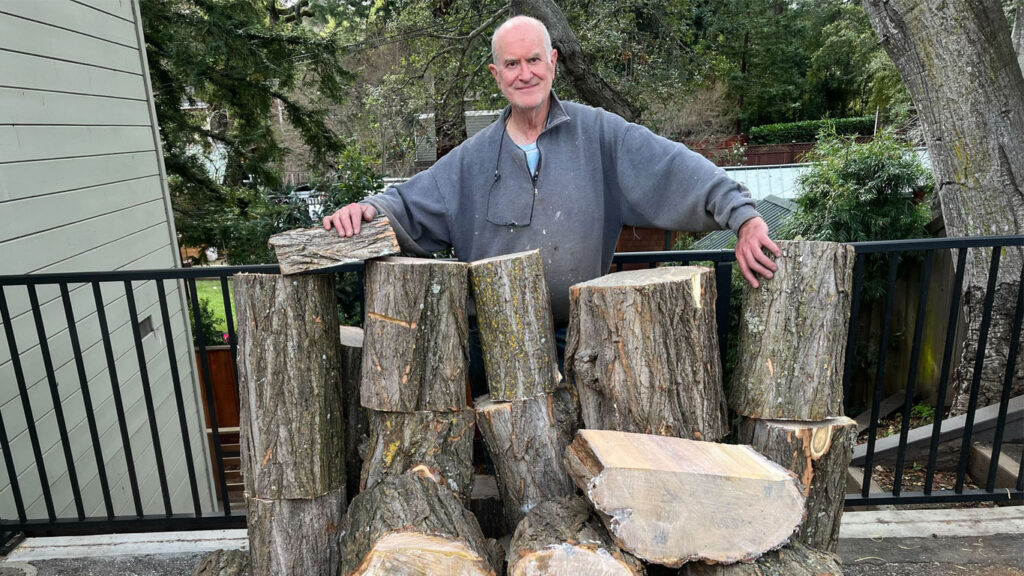 Edgar Whipple stays behind a large stack of wood for woodturning.