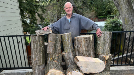 Edgar Whipple stays behind a large stack of wood for woodturning.