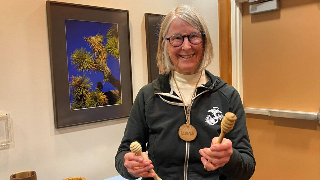 Luana shows two honey dippers that she turned on a lathe. She also wears her name badge.