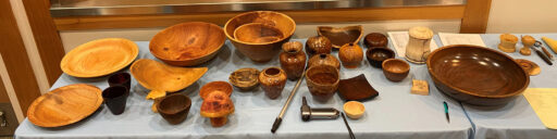 A table with dozens of woodturning projects, mostly bowls.