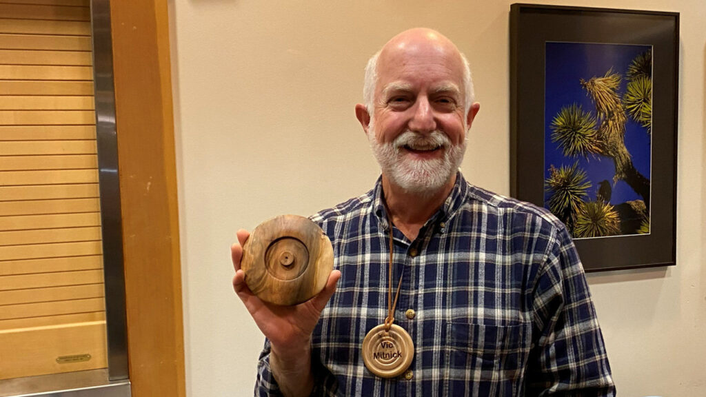 Vic shows a lid that he turned on a lathe. He also wears a round name badge.