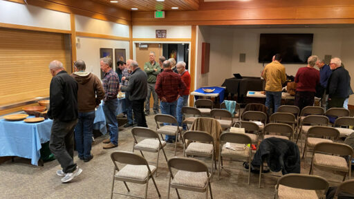 Members of the West Bay Woodturners club are socializing around tables with show-and-tell woodturning projects.