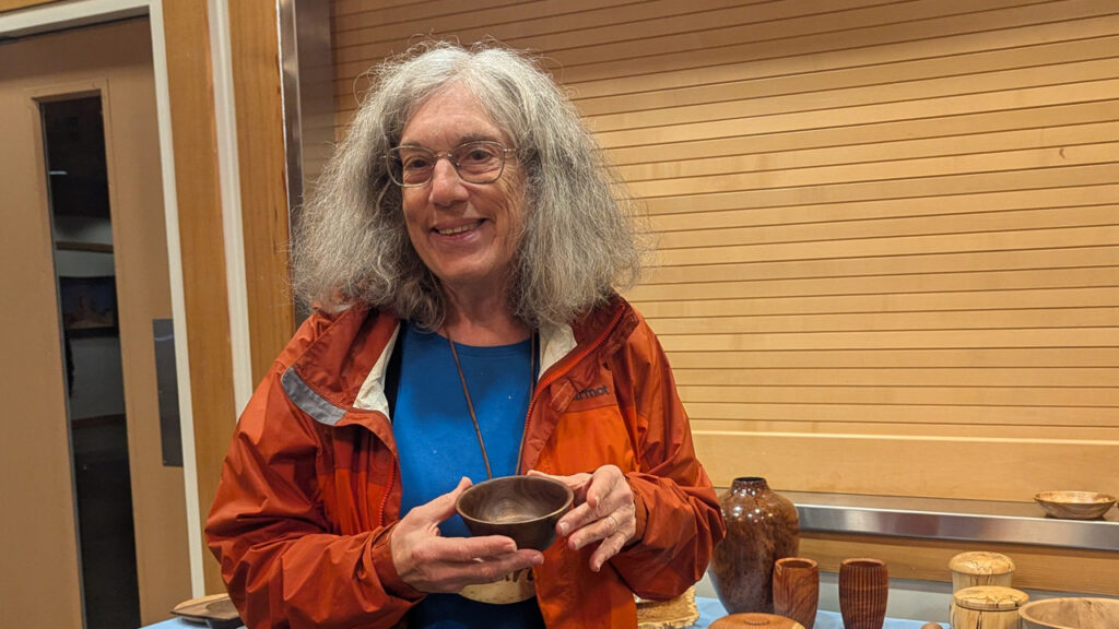 Laura is showing a small bowl that she turned from walnut wood on a lathe.