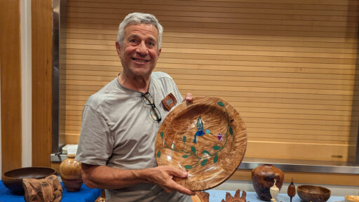 Bob is holding a maple burl platter with hummingbird stone inlay that he turned on a lathe.