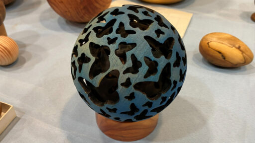 A hollow sphere with a butterfly design pierced and burned into it.