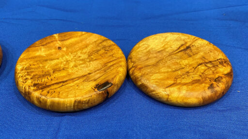 Two coasters turned from light-colored wood with beautiful grain by Jon Bishop on a lathe.