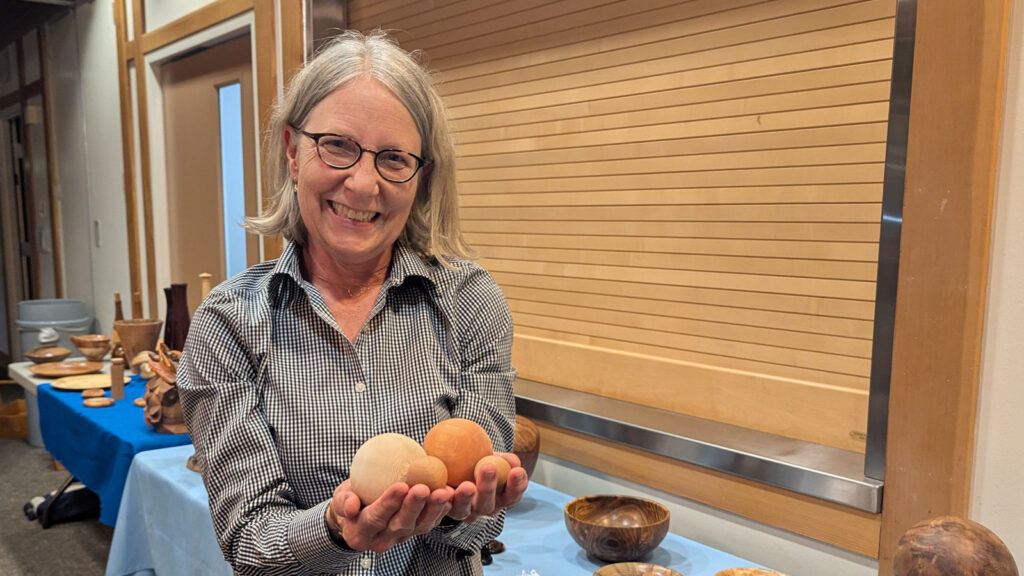 Kirsten is holding several wooden spheres that she turned on a lathe.