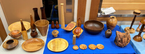 A display table full of woodturning items: platters, bowls, mushrooms, coasters, a lighthouse, and two pears.