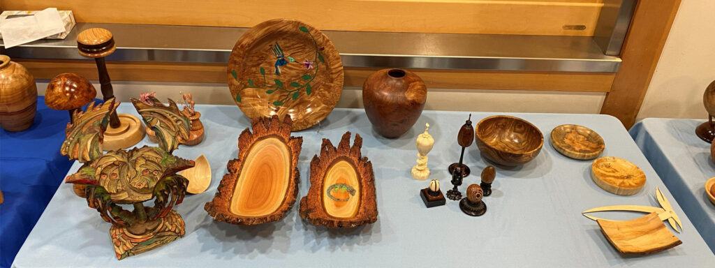 A display table with show-and-tell woodturning projects. Turned platters, bowls, vases, and wig stands.