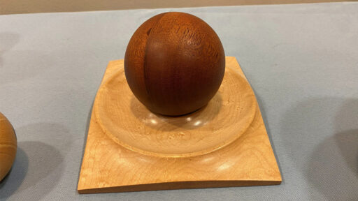 A dark-colored sphere on a light-colored square stand turned by Tom Gaston.