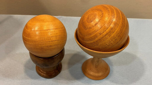 Two wooden spheres on their cup-stands that Tom turned on a lathe.