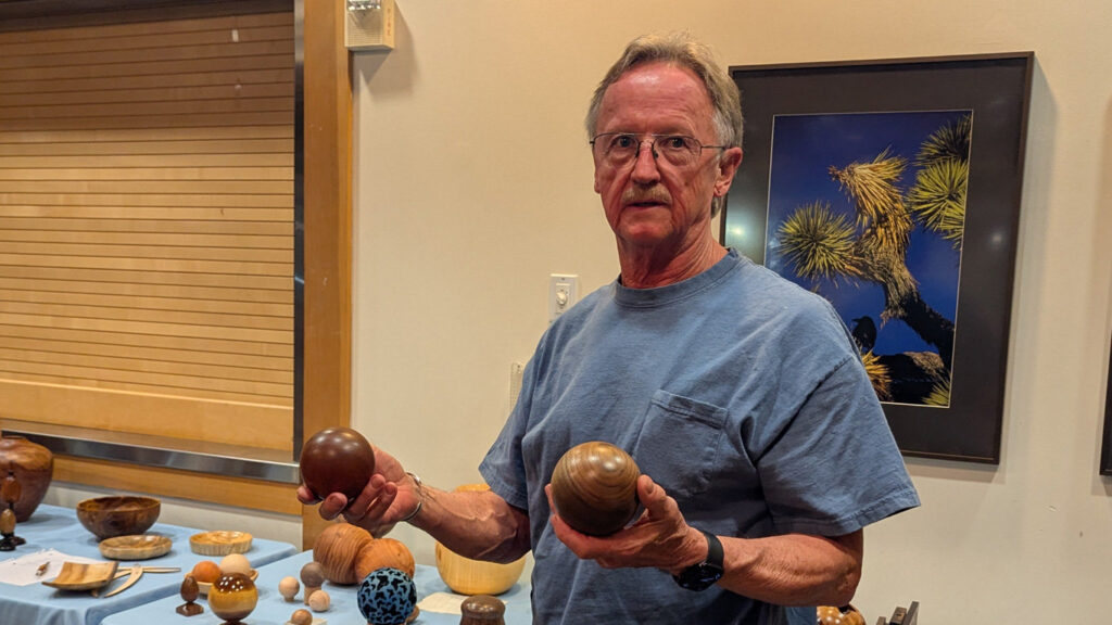 Tom is holding two wooden spheres that he turned on a lathe.