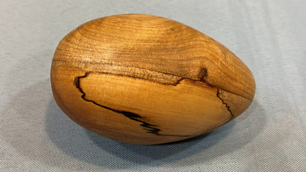A wooden egg turned by Vic on a lathe from unknown wood that shows spalting.