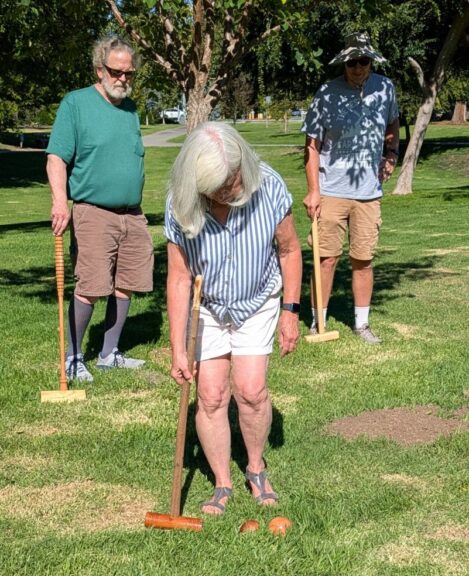 Carol Dahout playing croquet at the August 2026 WBW/SVW annual picnic while Steve Dahout and Mark Wedel look on.