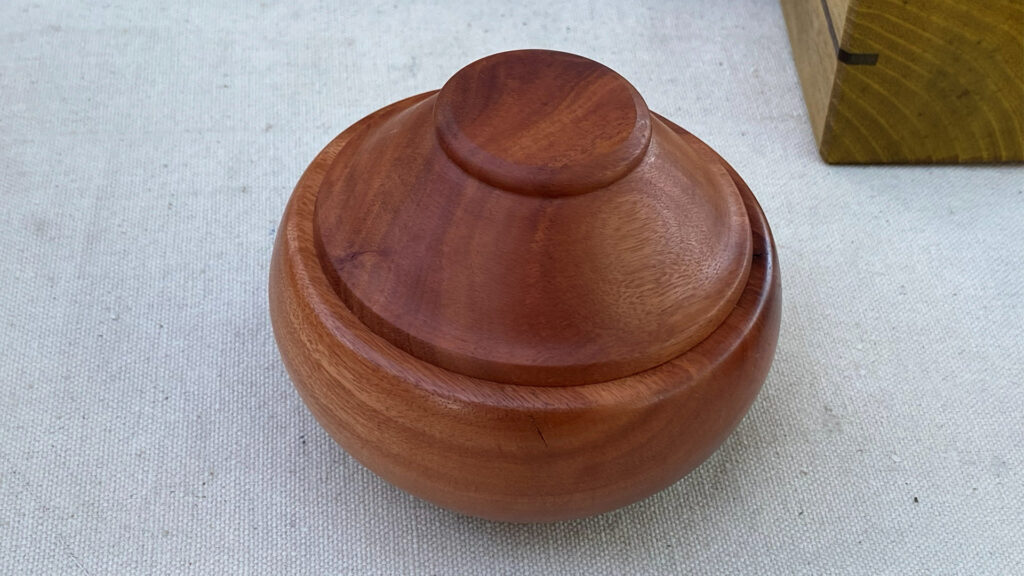 A round, reddish-brown wooden lidded vessel by Alison Lee.