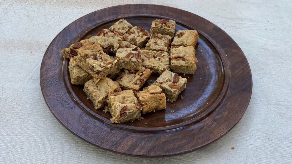 A dark, turned wood platter made by Daniel Saal, filled with a pile of square-cut nut bars.
