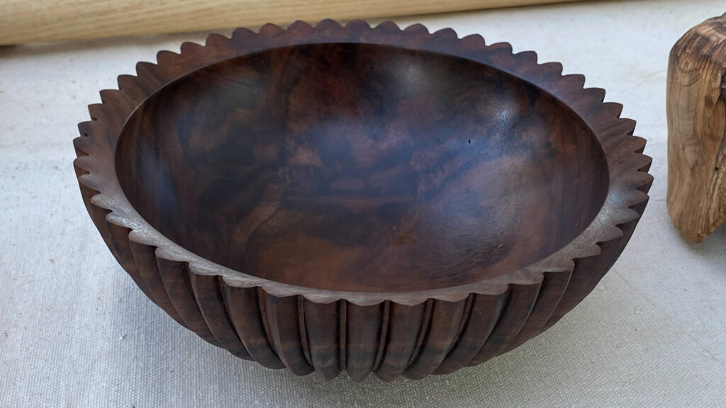 A dark wooden bowl featuring vertical flutes and a scalloped rim, turned and carved by Jon Bishop.