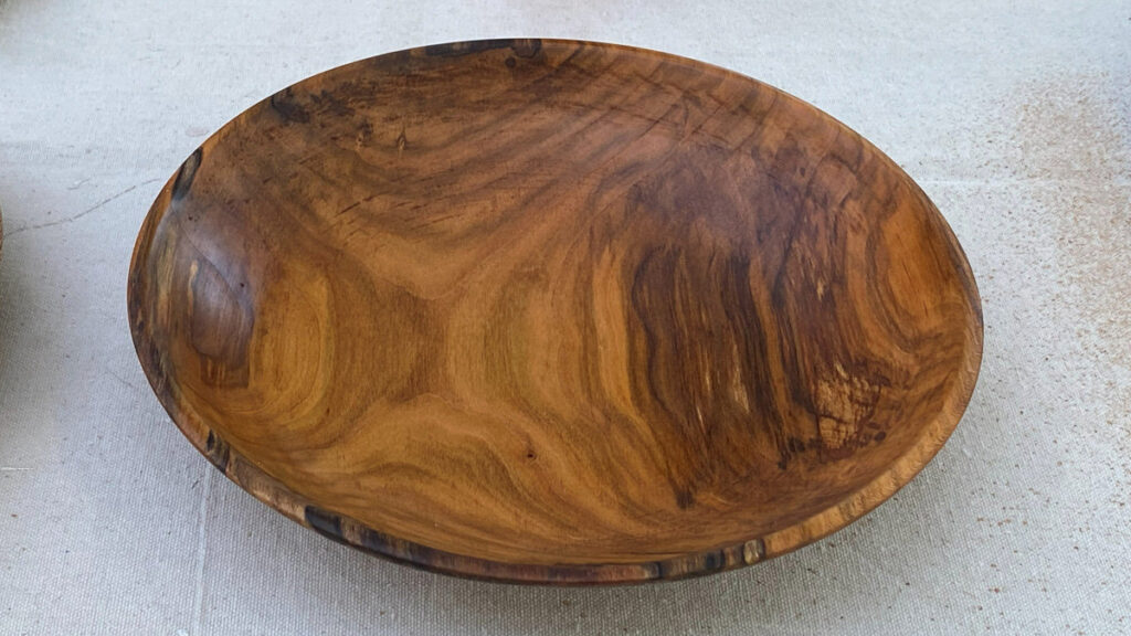 A turned wooden platter with a smooth, glossy finish and rich, swirling brown grain patterns. Turned by Kelly Smith from cherry wood.