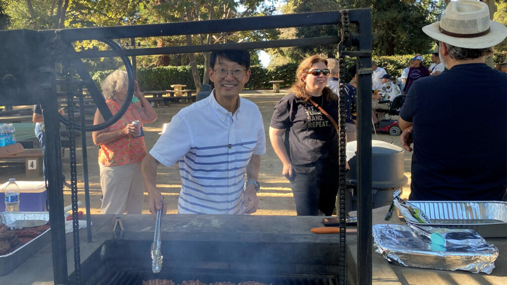 Sang Park smiles while grilling at the 2026 joint picnic of the Silicon Valley Woodturners and West Bay Woodturners clubs in Cuesta Park, Mountain View.