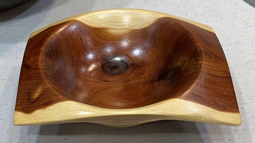 A polished, two-toned cedar bowl turned by Al Holstein, featuring a light rim and dark reddish interior, displayed at a West Bay Woodturning club meeting.