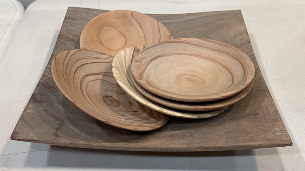 Shallow bowls by Alison Lee were displayed on a dark wooden platter, showcasing intricate grain patterns and concentric rings at a West Bay Woodturners meeting.