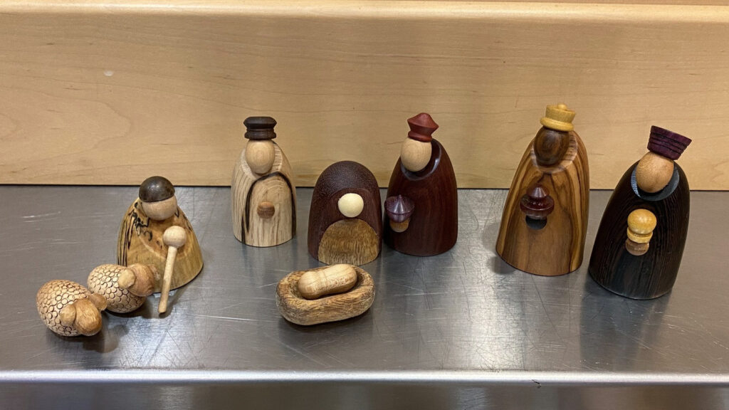 Angela Gunn's woodturned nativity scene, featuring hand-turned figures from various woods, including sheep and a manger, was displayed at the West Bay Woodturners' monthly meeting in Los Altos, CA.
