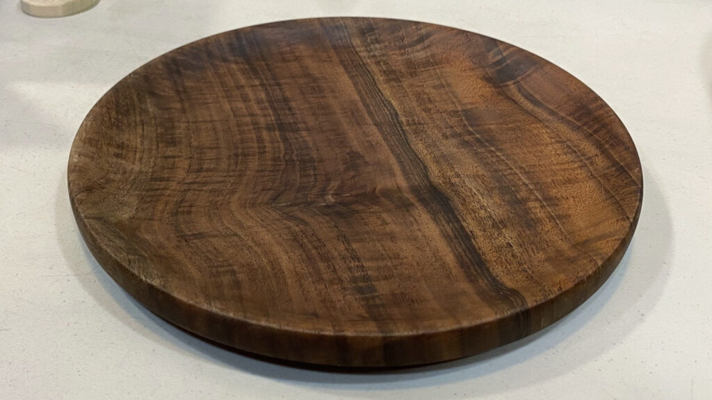 Bob Bley's hand-turned Bastogne walnut platter featuring rich, swirling grain and a glossy finish, displayed on a white table at a West Bay Woodturners meeting.