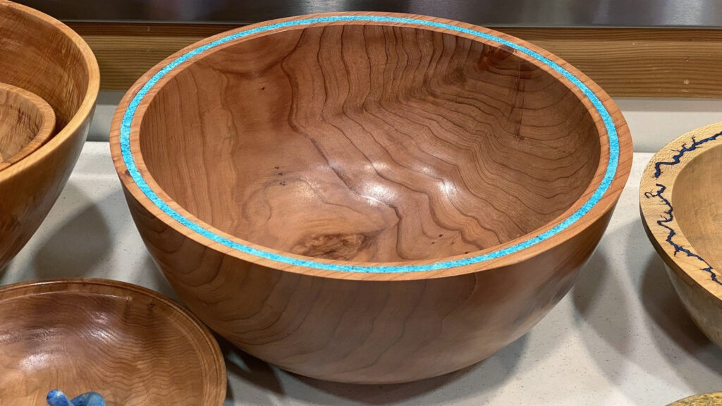 Large polished Redwood bowl with a turquoise rim by Bob Bley, displayed alongside other woodturning projects at a West Bay Woodturners Show & Tell event.