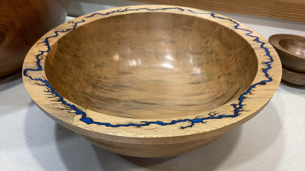 Polished Redwood bowl by Bob Bley featuring a bright turquoise resin inlay along the wide rim, displayed on a white speckled surface.