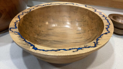 Polished Redwood bowl by Bob Bley featuring a bright turquoise resin inlay along the wide rim, displayed on a white speckled surface.