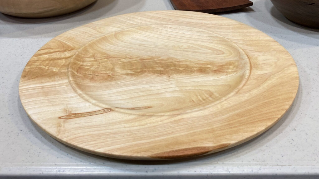 A Shamel Ash woodturning platter by Daniel Saal with swirling light grain, displayed on a white speckled countertop at a West Bay Woodturners meeting.