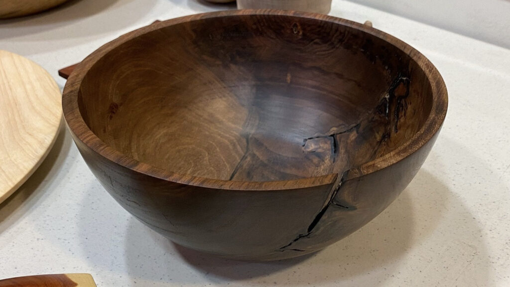 Hand-turned walnut bowl by Daniel Saal featuring natural cracks and rich grain, displayed on a speckled white countertop at a West Bay Woodturners meeting.