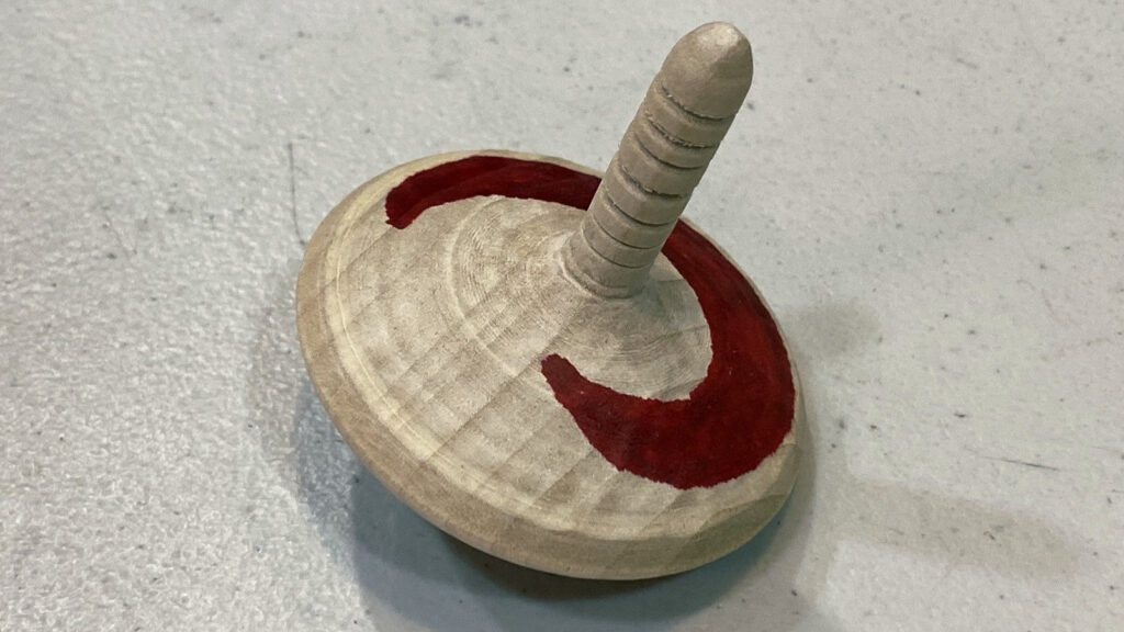 Wooden spinning top by Kirsten Mouradian with a red crescent design representing a sickle cell. When spun, the decoration appears round, illustrating how medication restores blood cells in pediatric patients.