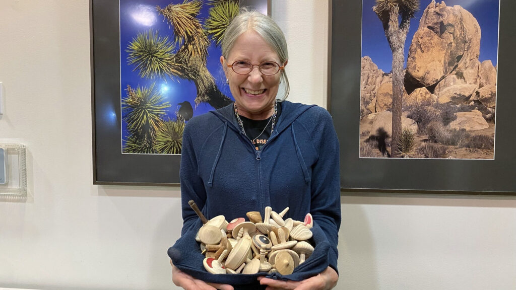 Kirsten Mouradian holds a collection of donated wooden spinning tops at a West Bay Woodturners meeting. These tops help pediatric sickle cell anemia patients visualize how medication restores red blood cells to their round shape.