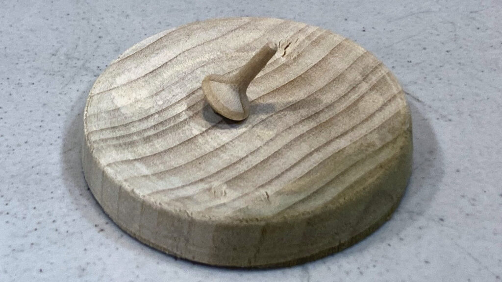 Tiny hand-turned wooden spinning top by Kirsten Mouradian resting on a poplar spinning base. The light-colored wood features visible concentric lathe marks.
