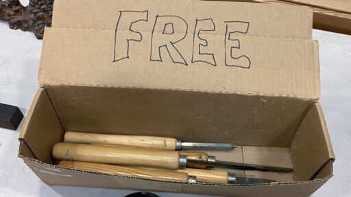 Woodturning chisels and a dark burl serving as participation prizes in a box labeled FREE at a West Bay Woodturners meeting in Los Altos, California.