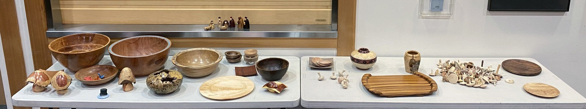 Hand-turned wooden bowls, platters, and spin tops displayed on a table during a West Bay Woodturners monthly meeting in Los Altos, California.